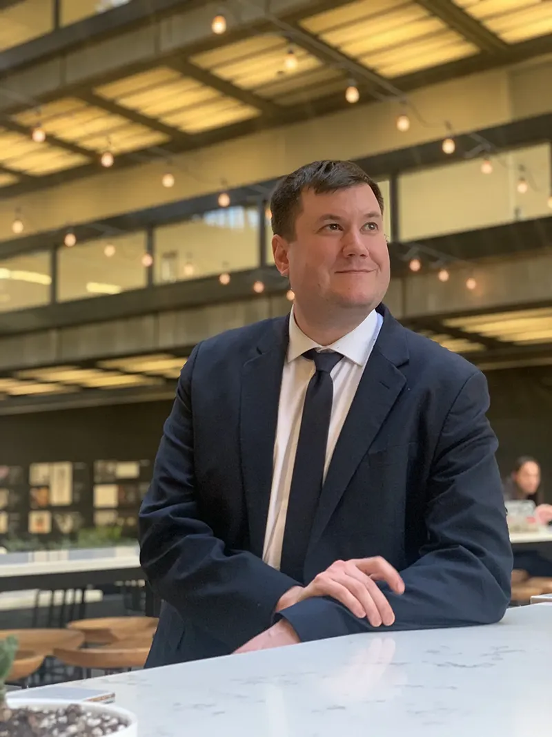 Matthew De Nero seated in a suit in a modern indoor space